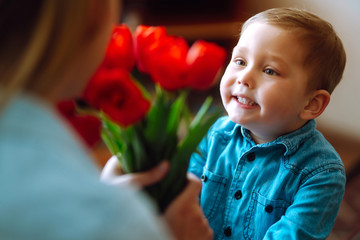 Fototapeta premium Little son congratulates mother and gives a bouquet of flowers tulips. Happy mother's day. Family holiday and togetherness.