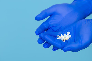 The pills are in the doctor's hands. Hands in blue medical gloves hold pills. Blue isolated background.