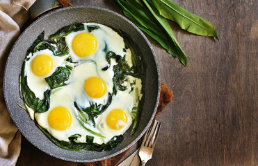 fried eggs with wild garlic as a shakshuka. fried eggs in a frying pan under gray marble on a table, top view. Keto diet dish