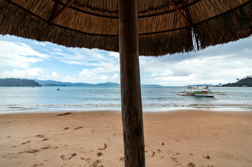 Fototapeta na wymiar Seascape shot in a cloudy day from under a straw umbrella in the beach of Port Barton, Palawan, Philippines