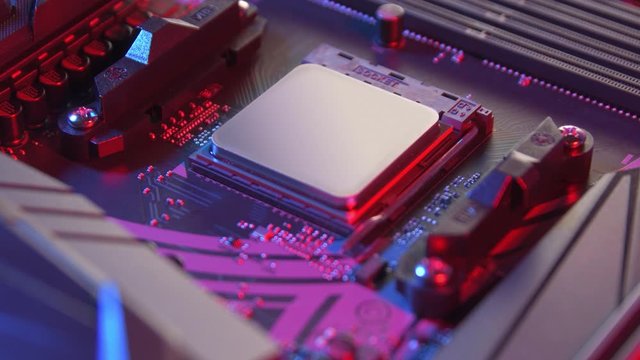 Motherboard with processor close up tilt shot. Computer components on circuit board lit with red and blue ligths.