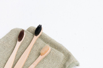 three bamboo toothbrushes on a coarse green natural fabric, white background copy space, top view