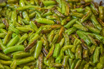 Fresh juicy green french beans are fried in a frying pan on a kitchen gas stove