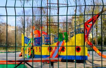 An empty playground across the metal fence, which is forbidden to visit during the quarantine period of the pandemic of COVID-19 disease caused by coronavirus