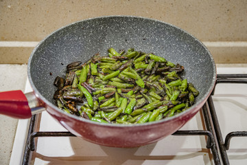 Fresh juicy green french beans are fried in a frying pan on a kitchen gas stove