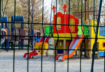 An empty playground across the metal fence, which is forbidden to visit during the quarantine period of the pandemic of COVID-19 disease caused by coronavirus