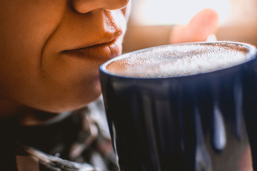 person holding blue cup of hot aromatic coffee and taking a sip