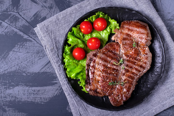 Grilled beef steak served on the stone plate with lettuce leaf and cherry tomatoes
