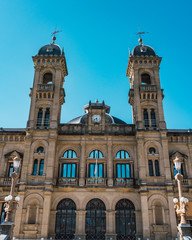 Fototapeta premium Town hall of the city of san sebastian in donostia, guipuzcoa, basque country, Spain, with two dark colored domes with pointed ends and a central clock. The sky is blue and cloudless. 