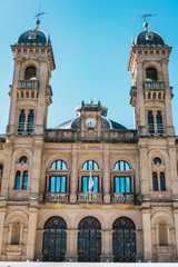 Fototapeta na wymiar Town hall of the city of san sebastian in donostia, guipuzcoa, basque country, Spain, with two dark colored domes with pointed ends and a central clock. The sky is blue and cloudless. 