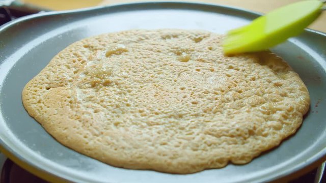 Butter brush smear pancake on hot pan gas stove in kitchen. Slowmo closeup