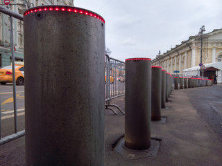 A long row of retractable metal bollards with hydraulic lift for traffic control, equipped with red LEDs on the upper end
