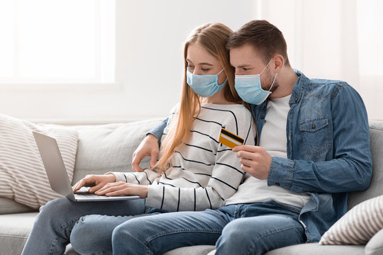 Young Couple In Protective Masks Ordering Food With Laptop And Credit Card At Home