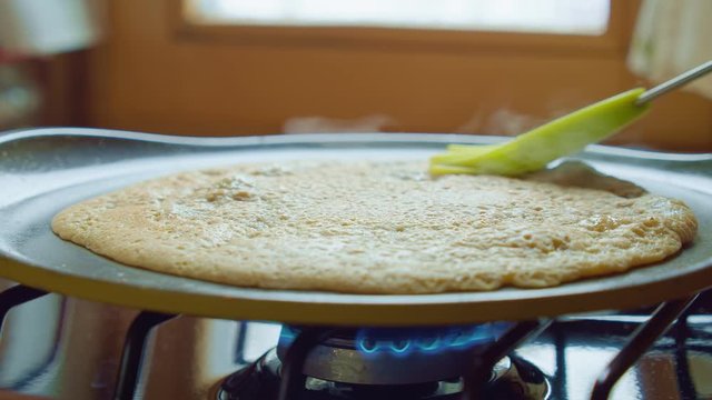 Butter brush spreads pancake on hot pan gas stove in kitchen. Slowmo closeup