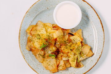 Homemade fried potatoes with spices and sour cream on a white plate