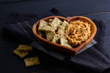 Hummus with cracker in a bowl on a dark table