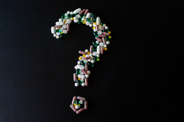 A question mark laid out of pills in the center of the black matte background. photo with selective focus. Medical pharmacy background. Copy space.