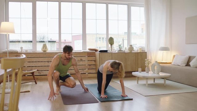 Fit young adult Caucasian couple living together practicing yoga at home. Girlfriend teaching boyfriend how to do yoga. Stay home, quarantine workout. Shot on ARRI Alexa Mini