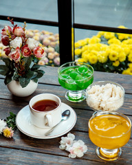 a cup of tea served with three bowls of jams