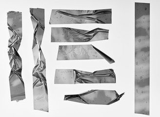 Metallic sticky teared tape shapes cuts isolated on white background. Shiny flexible crumpled...