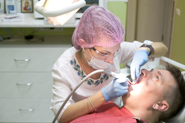A female dentist in a pink sterile hat and white coat is treating a man’s teeth. Inspection at the dentist. Dental treatment. Implantation and whitening