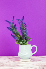 Lavender flowers in a pastel blue mug on a marble table and purple background