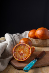 Close-up of blood oranges with blue knife and dishcloth on wooden table and black background in...