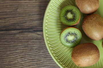 Still life. Whole and cut kiwi on a green plate with a wooden background.