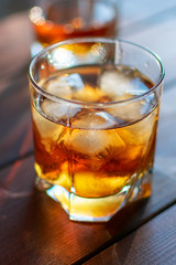 Two glasses of whiskey with ice cubes served on wooden planks.