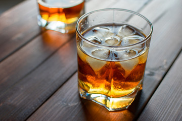 Two glasses of whiskey with ice cubes served on wooden planks.