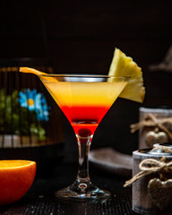 a martini glass with orange cocktail garnished with orange and pineapple