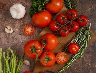 Red tomatoes, thyme, rosemary, garlic, parsley and asparagus on rustic rusty background