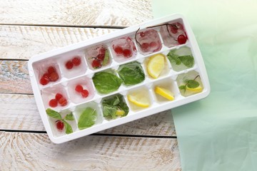 Obraz na płótnie Canvas Ice cubes with mint, lemon and red berries in a tray for making drinks, dessert, healthy food 