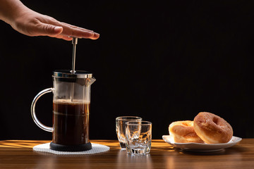 Coffee brewing in a French press pot and two donuts in plate on the wood table and warm morning light, Selective focus.