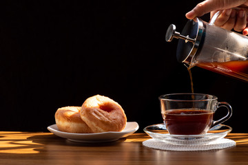 Coffee brewing in a French press pot and two donuts in plate on the wood table and warm morning...