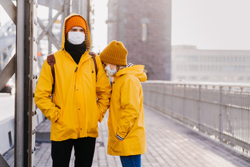 Couple in surgical face masks dressed in yellow jackets, confused because of the coronavirus are...