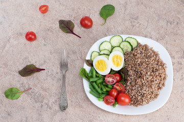 Tasty and healthy food from natural products. Salad of green vegetables, tomato and buckwheat in a white plate. Buckwheat with vegetables and eggs on a white plate.