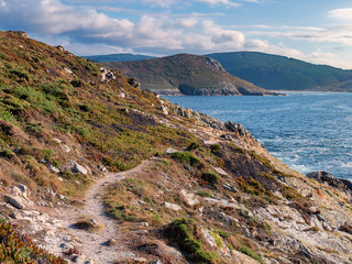 Camiño dos faros, the Lighthouse Trail, at Laxe, passing hillside over a narrow path above rocks...