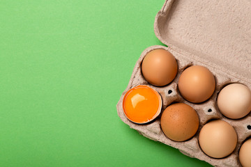 Egg tray on bright green background with broken egg, 
egg yolk, copy space, top view.
