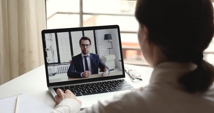 Confident businessman online coach, mentor wearing suit video calling by webcam in conference chat professional training talking to client interviewing candidate on laptop screen. Over shoulder view.