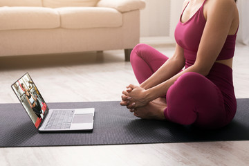 Online yoga class. Unrecognizable woman in lotus pose meditating near laptop at home