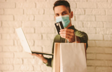 Happy man in protective face mask shopping in online internet store. Young hipster man in medical...