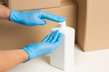 Obraz premium Deliveryman disinfects hands. Cardboard boxes at background