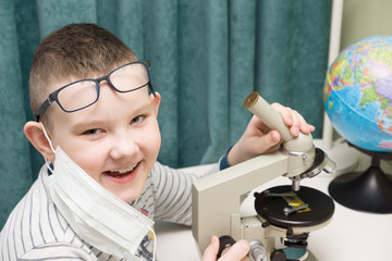 boy in a protective mask studies a microscope