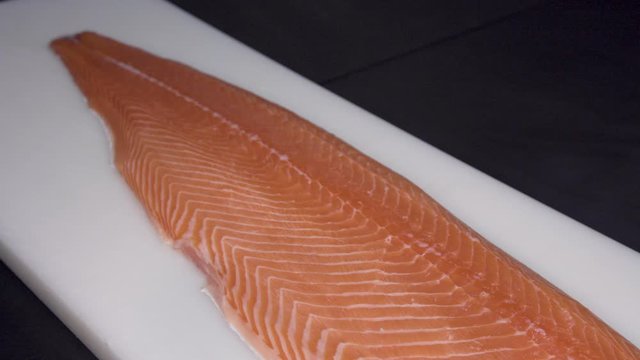 Closeup of a Salmon Fillet on a white cutting board on a black table 