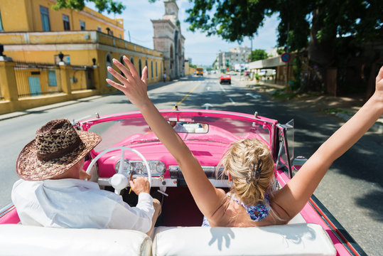 Rear view of happy friends enjoying in the convertible car drive through Havana