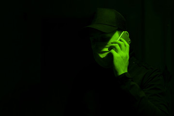 Young man with a mask looking down making a phone call under green light