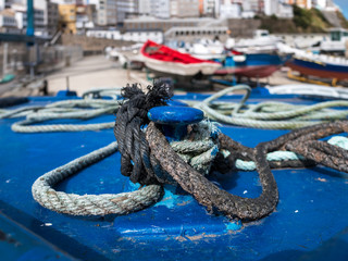 Close-up of ropes on a cleat and fisher boats in the blurred background in the harbor of Malpica de...