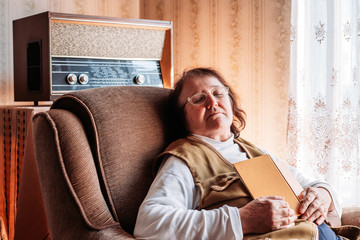 Elderly woman holding a book, napping in the chair by the window.