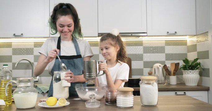 Two girls preparing cookies together in kitchen. Children sift flour through sieve